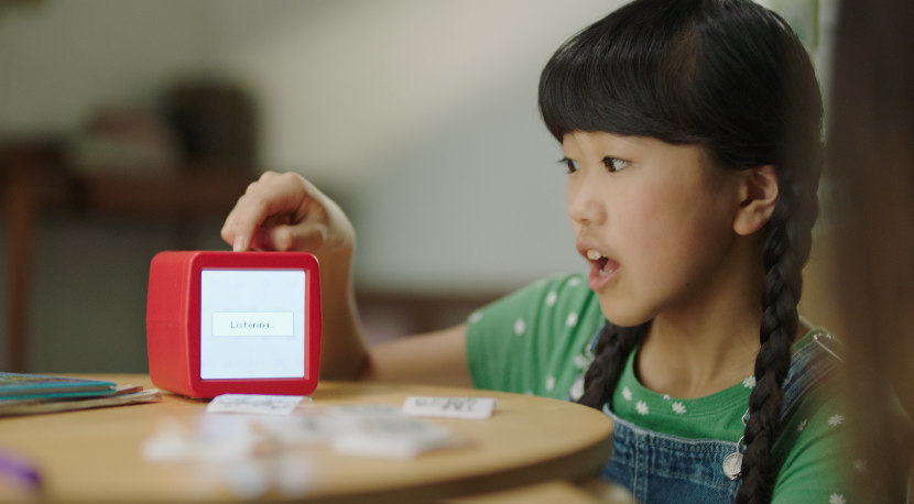 A child speaking into Stickerbox printer, and the Stickerbox is showing "Listening" on its screen.